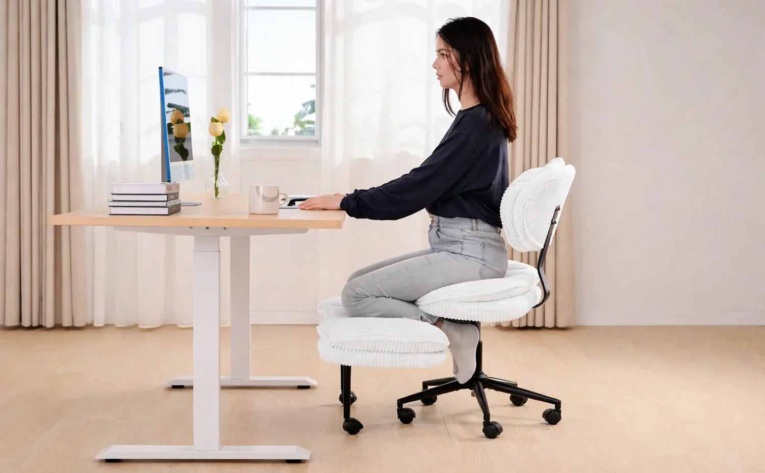 A woman maintaining good posture while sitting on a white cross-legged ergonomic office chair at a wooden standing desk.